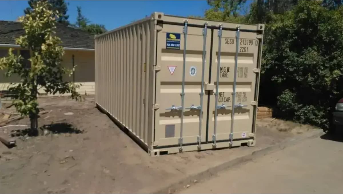 A beige shipping container on a dirt lot.