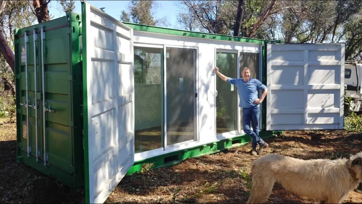 A man standing beside a shipping container house.