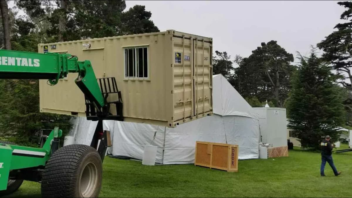 Forklift placing a modified beige shipping container with a window onto a site