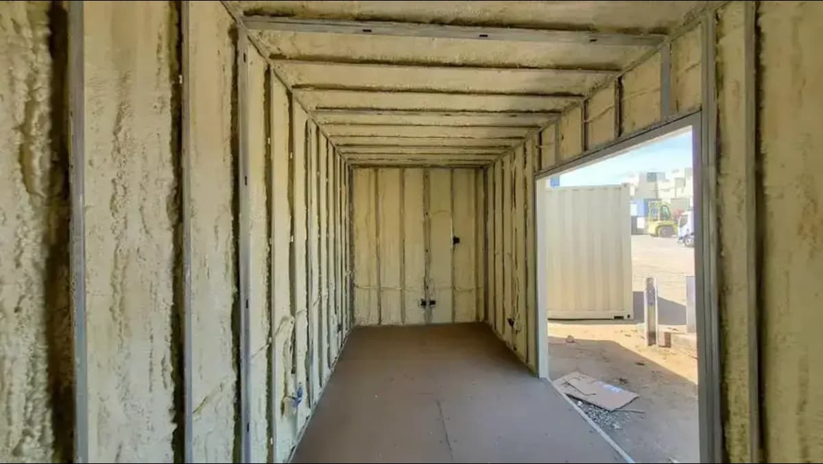 The interior of a shipping container with walls stripped away, exposing the spray foam insulation