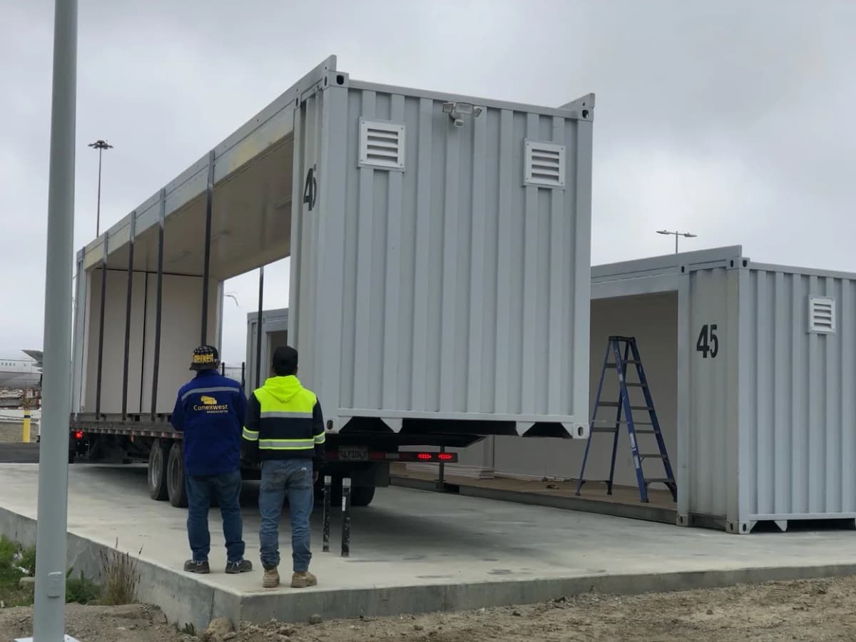 Two workers standing near a container as it is being installed onto a concrete platform