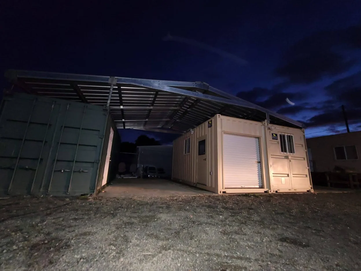A steel truss roof structure mounted over shipping containers