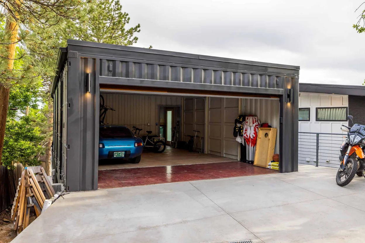 Modern garage made from a repurposed black shipping container with a wide roll-up door.