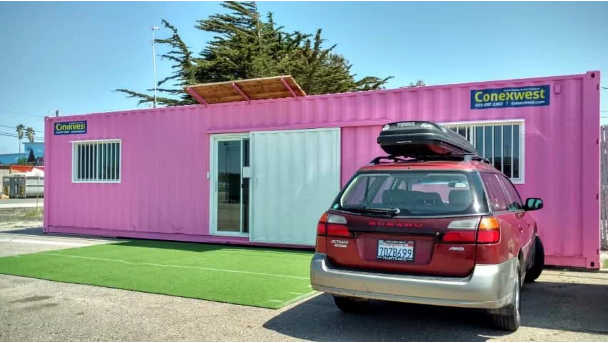 Pink container home in with a red Subaru parked in front of it