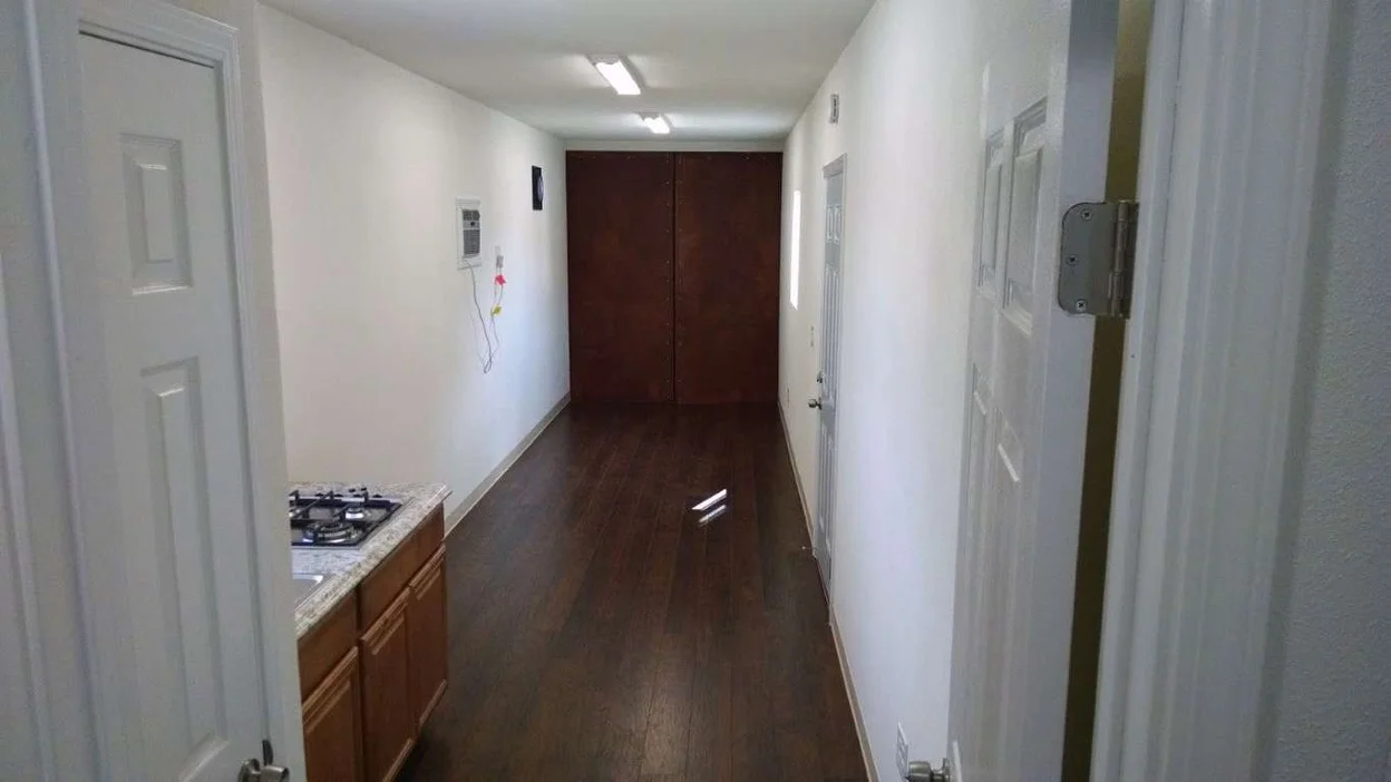 The interior of a refurbished container home with wooden flooring, countertops, stovetops, and doors.